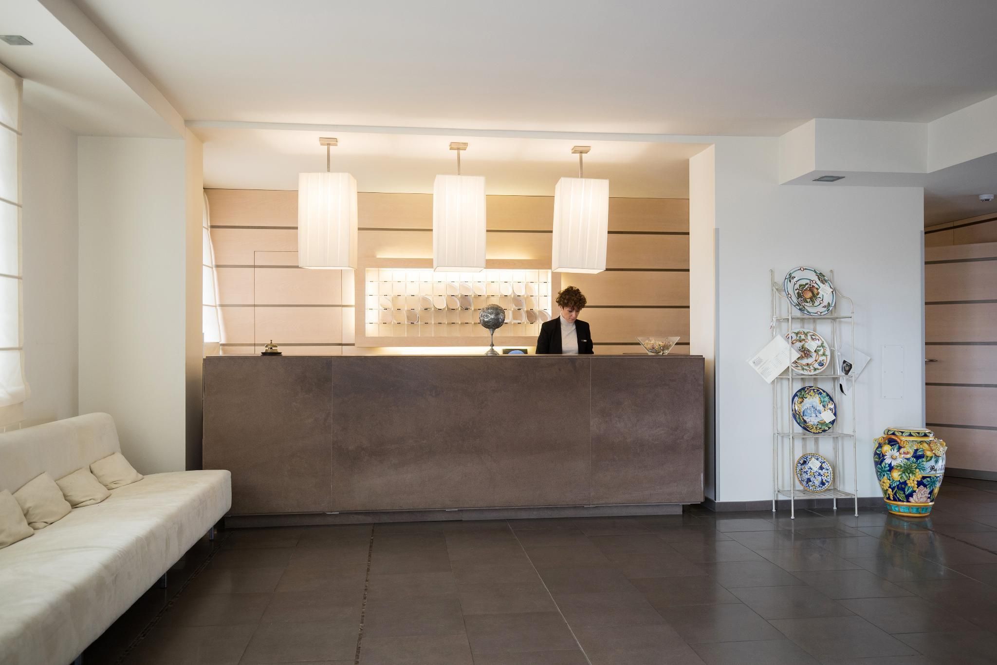 Zona reception di un hotel dal design moderno, con scrivania, divano e una rastrelliera decorativa.