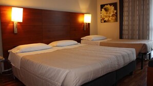 Habitación de hotel con tres camas, cabecero de madera, lámparas de pared y un cuadro floral.