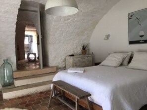 A bedroom with a large bed, a bench, a dresser, and a hanging light fixture. - Charming stone residence with heated swimming pool 4X10 (Saint Pantaléon)
