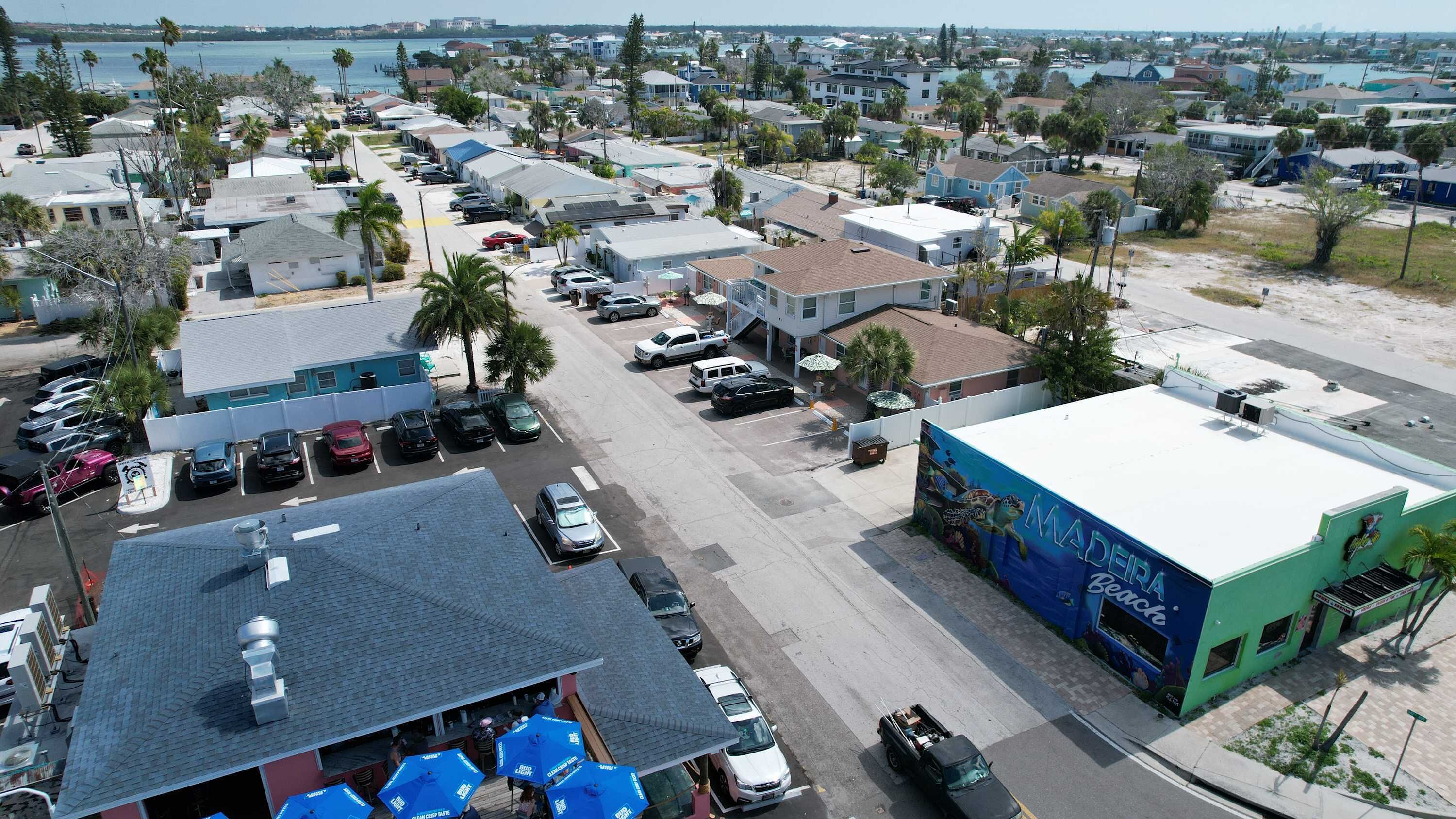 A coastal area with a row of single-story buildings, a parking lot, and a beach in the background.
