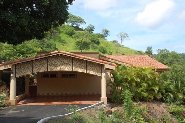 A building with a covered entrance and a tiled roof, surrounded by lush greenery and hills.