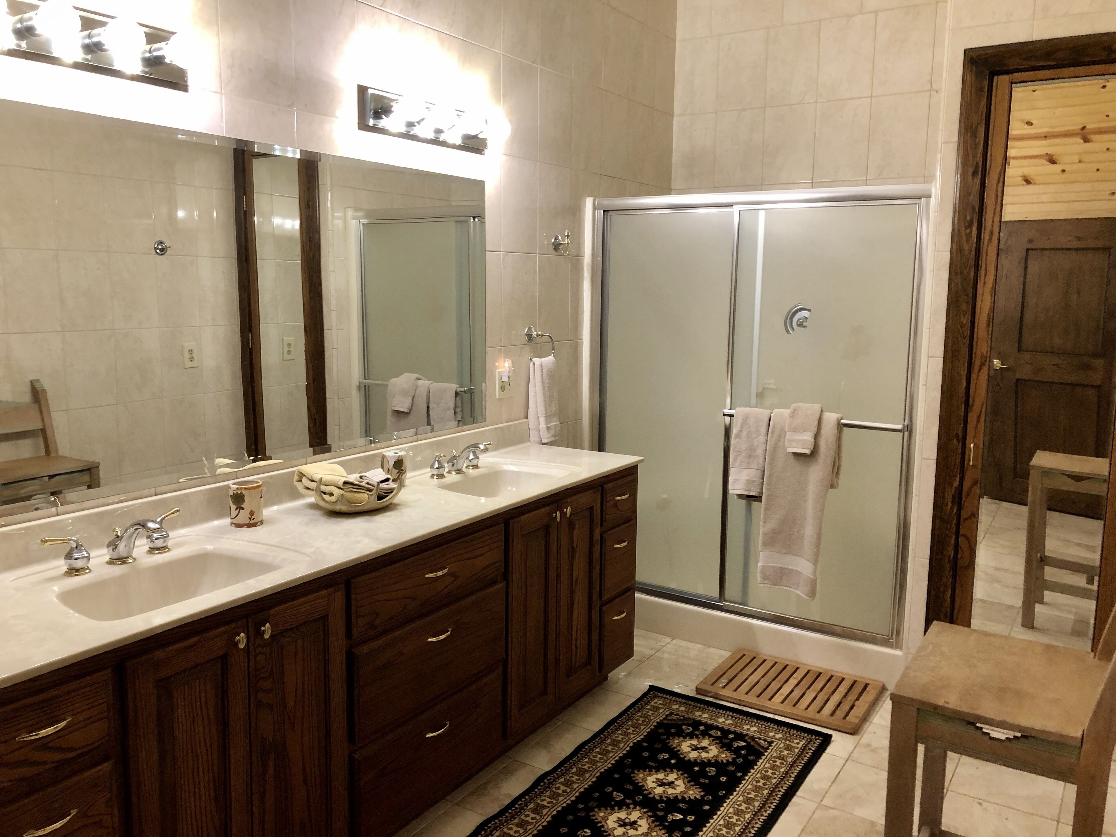 A modern bathroom with a double sink vanity, a glass shower enclosure, and a wooden bench.