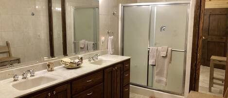 A modern bathroom with a double sink vanity, a glass shower enclosure, and a wooden bench.
