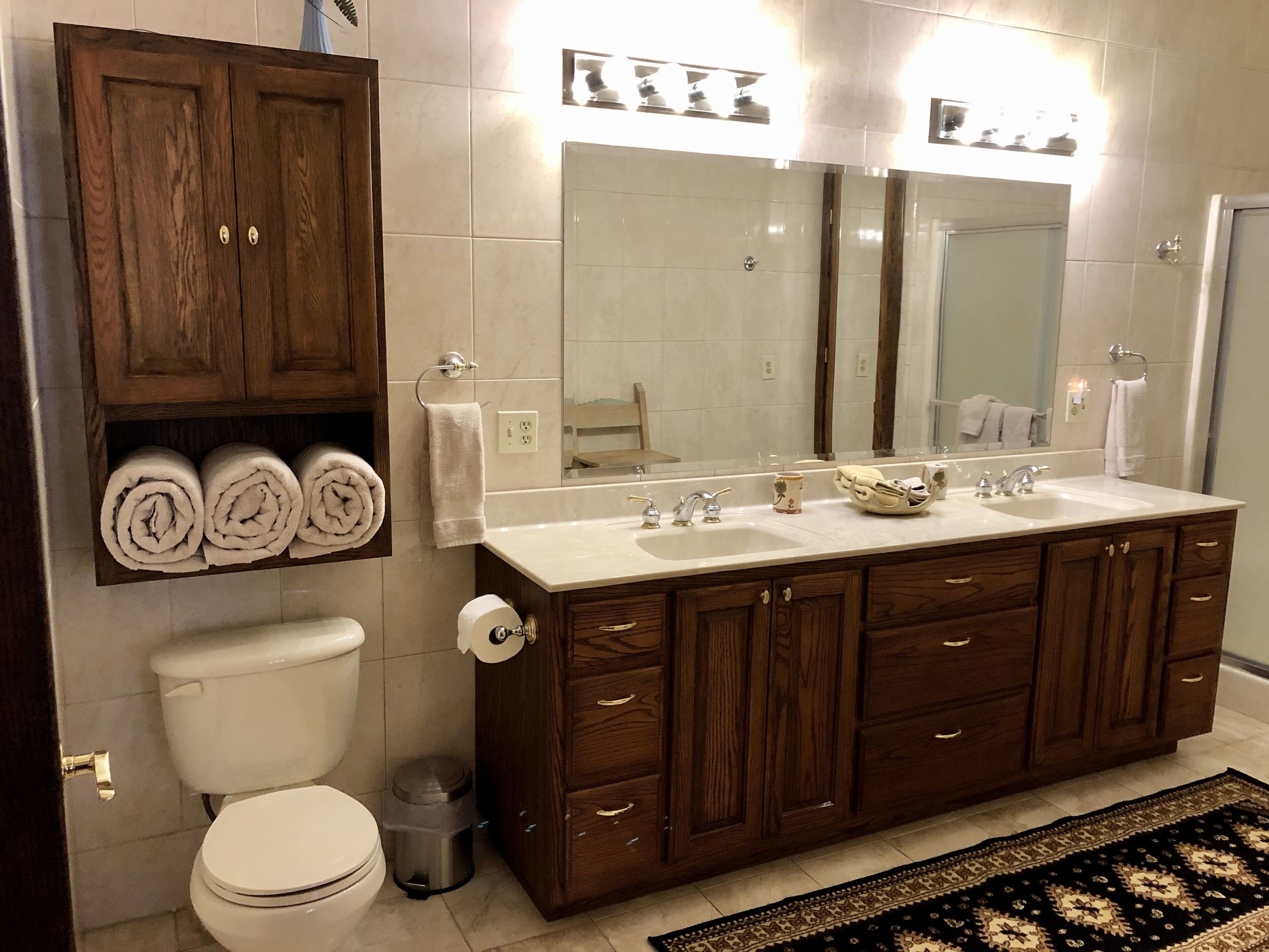 Een badkamer met een houten wastafelmeubel, een grote spiegel, een witte wasbak en een toilet.