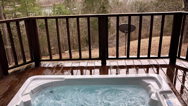 A hot tub on a wooden deck with a view of a river and hills.