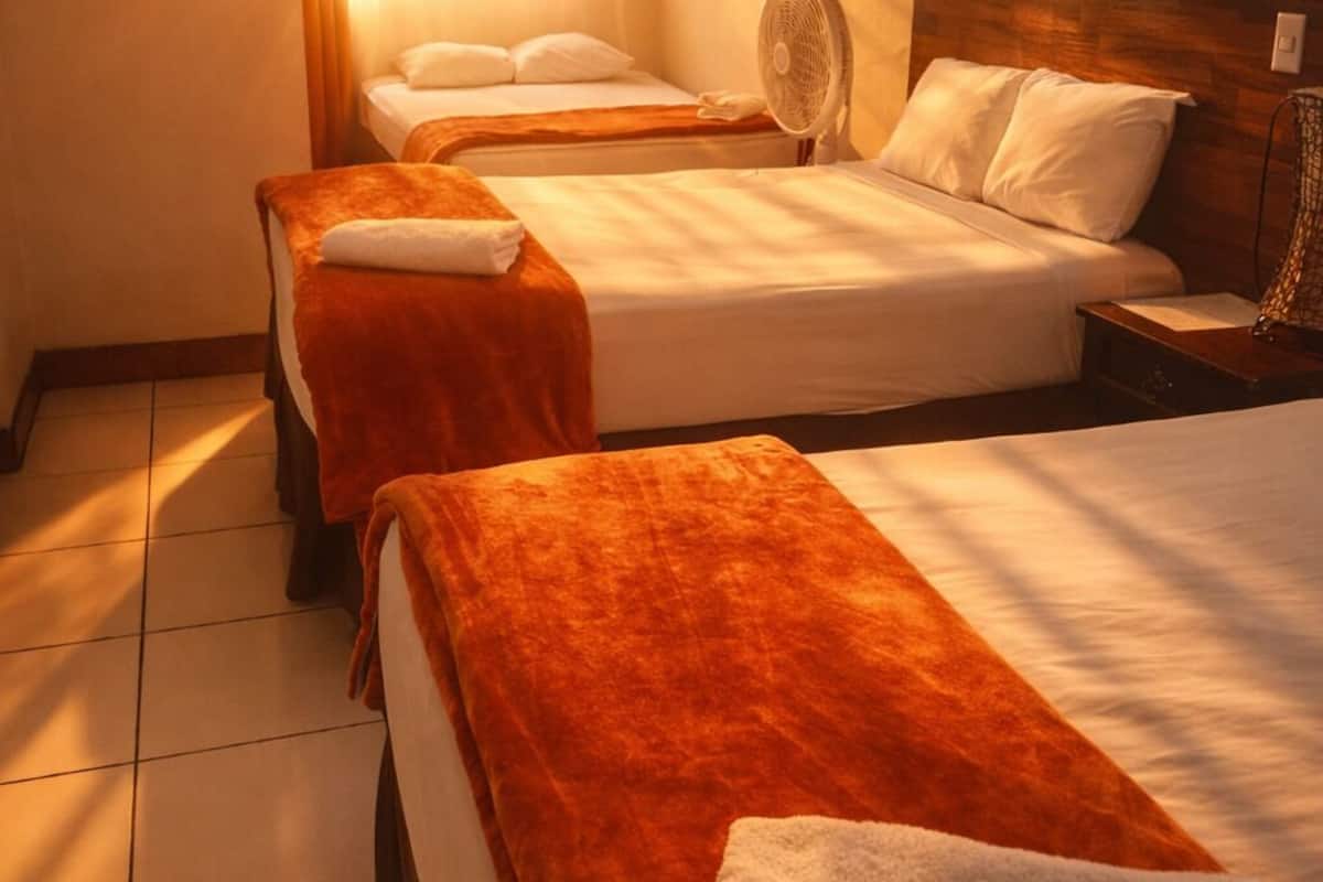 Quarto de hotel com duas camas, um ventilador e uma janela com cortinas.