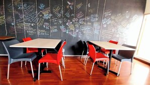 Uma sala de reuniões com quadro negro repleto de anotações manuscritas, cadeiras vermelhas e cinzas e piso de madeira.
