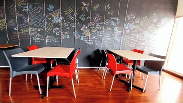 A meeting room with a blackboard filled with handwritten notes, red and grey chairs, and wooden flooring.