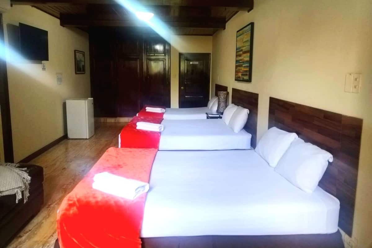 Quarto de hotel com duas camas, um refrigerador pequeno e teto de madeira.