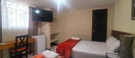 Habitación de hotel con dos camas, un escritorio, una silla, un televisor y una puerta.