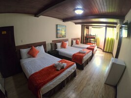 A hotel room with three beds, each with a red blanket and white pillows. There is a painting on the wall, a ceiling light, and a door with a sign.