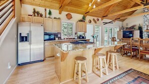 A spacious kitchen with a large island, wooden ceiling beams, and a stone accent wall.