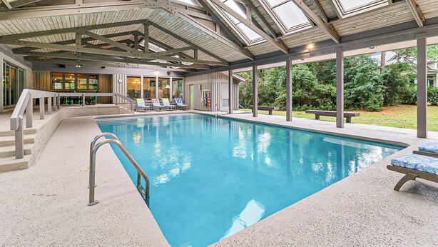 An indoor swimming pool with clear blue water, surrounded by lounge chairs and a covered seating area.