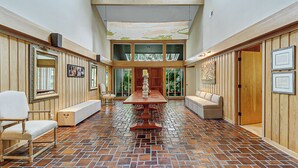 A spacious room with a brick floor, wooden paneling, a long table, and seating areas.
