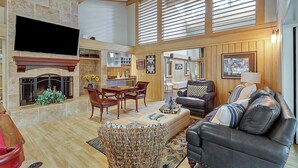 A spacious living area with a fireplace, wooden beams, a dining table, and comfortable seating.