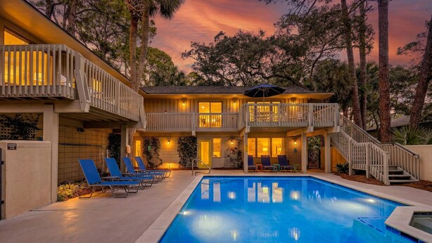 Uma casa de dois andares com piscina, área de estar externa e escadaria para uma varanda.
