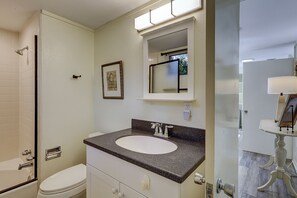 Een badkamer met een wit toilet, een wastafel met een granieten blad, een spiegel boven de wastafel, en een douchehoek.