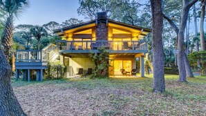Une maison à deux étages avec un balcon, entourée d’arbres et dont le sol est recouvert de feuilles.