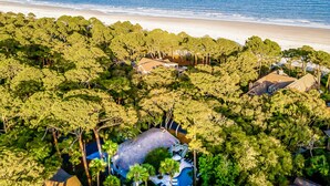 Vue aérienne d’une propriété située sur la côte, caractérisée par une végétation luxuriante, une plage et plusieurs maisons.