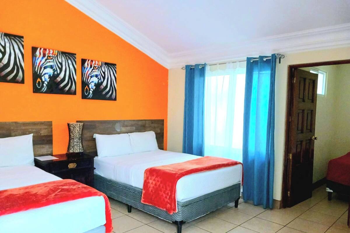 A hotel room with two beds, a wooden headboard, a nightstand, a vase, and three zebra paintings on the wall.