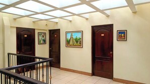 Un pasillo con tragaluces, puertas de madera y cuadros en las paredes.