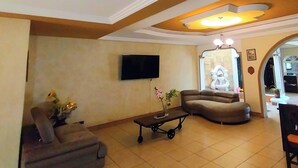 Amplia sala de estar con un sofá grande, una mesita y un televisor montado en la pared.