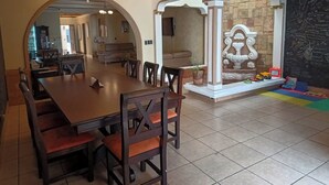 Un comedor con una larga mesa de madera y sillas, un arco que da a otra habitación y una pared de piedra decorativa con una fuente.