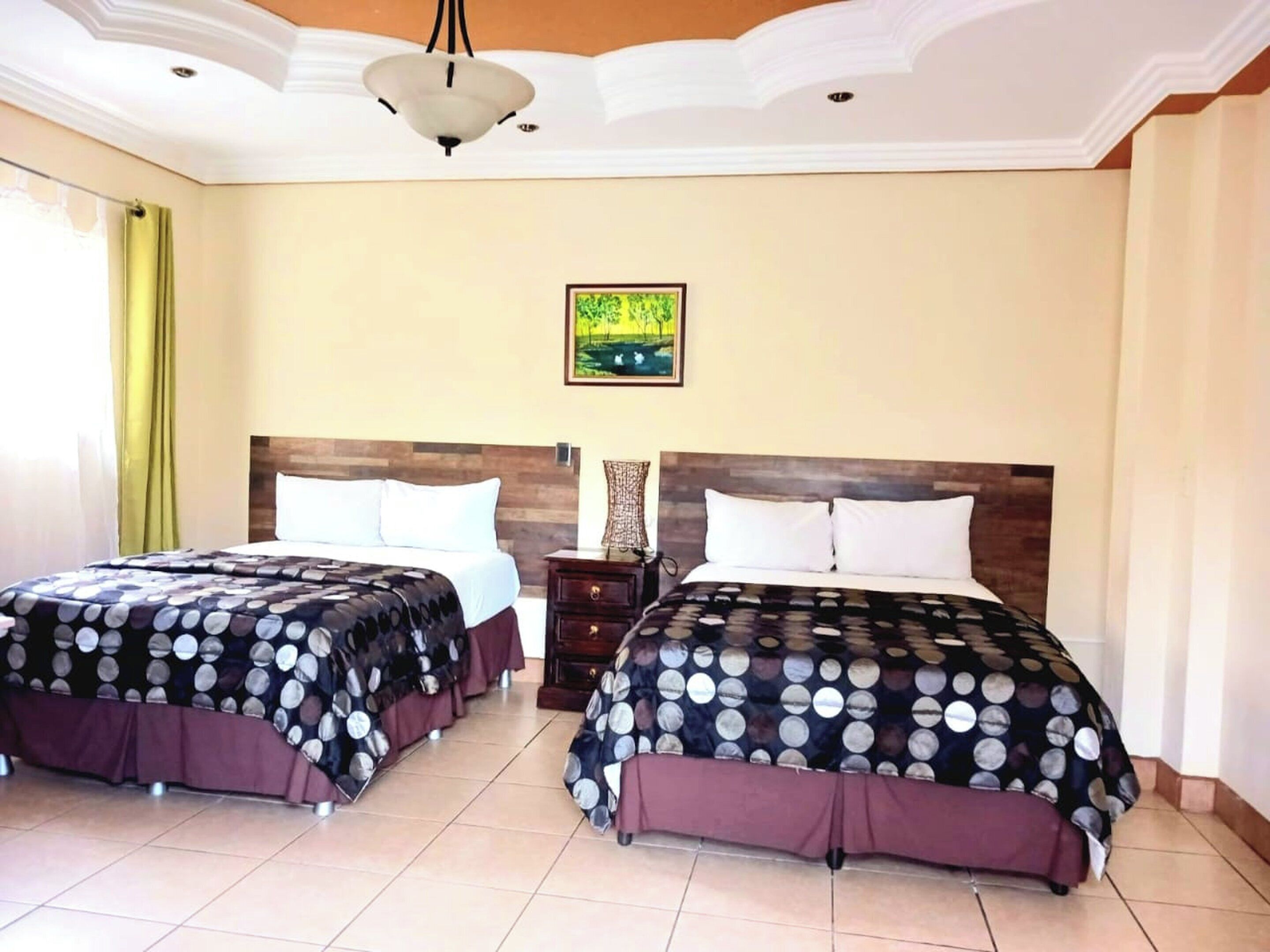 A hotel room with two beds, a wooden headboard, a painting on the wall, and a chandelier.