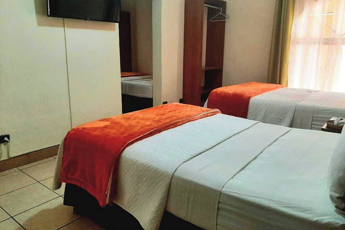 A hotel room with two beds, a wardrobe, a television, and a window with curtains.