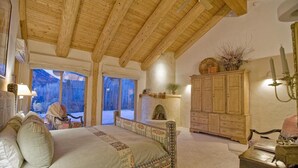 Un dormitorio acogedor con una cama grande, vigas de madera en el techo, una chimenea y vistas a un paisaje nevado.