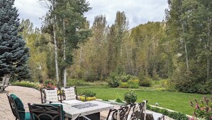Un patio al aire libre con mesa y sillas, rodeado de un jardín y árboles.