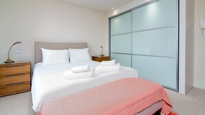 A modern bedroom with a large bed, wooden nightstands, a bedside table, and a large sliding glass door. - GuestReady - Spacious Apartment in Clapham Town (London)