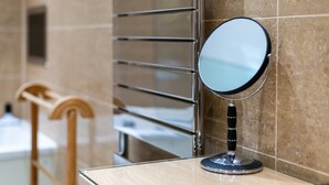 A bathroom with a round mirror on a wooden counter, a towel rack, and a tiled wall. - GuestReady - Spacious Apartment in Clapham Town (London)