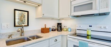 A kitchen with white cabinets, a stainless steel sink, a microwave, an oven, and a framed artwork on the wall.