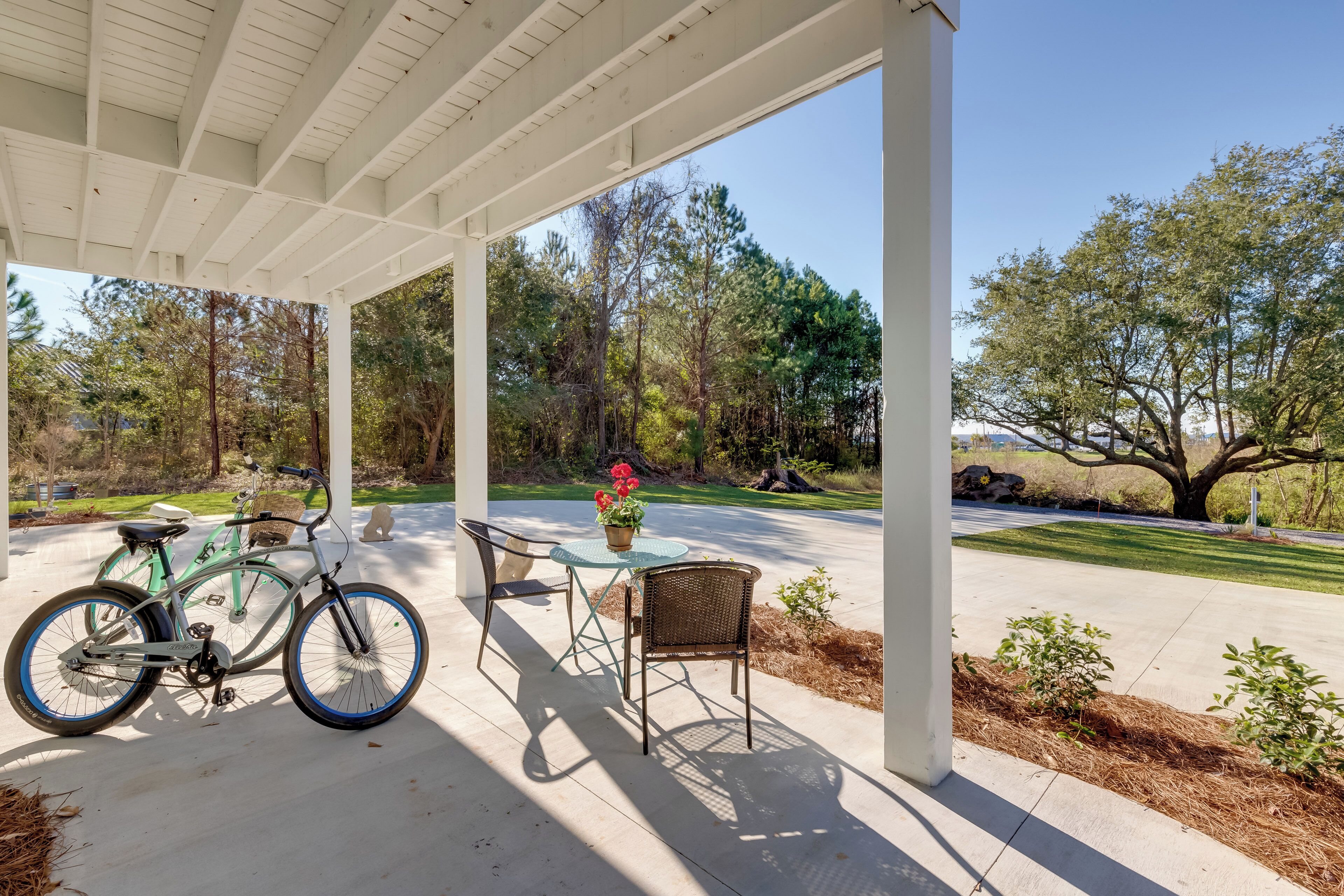A covered patio with a bicycle, a table with chairs, and a view of a wooded area.