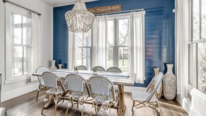 A dining room with a blue wall, white curtains, a chandelier, and wicker chairs. - Carlton Landing! Gorgeous Home on Redbud Park (Carlton Landing)