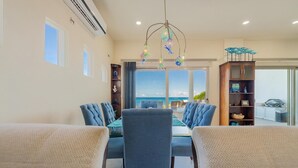 A dining area with a large table and chairs, a chandelier, and a view of the ocean.