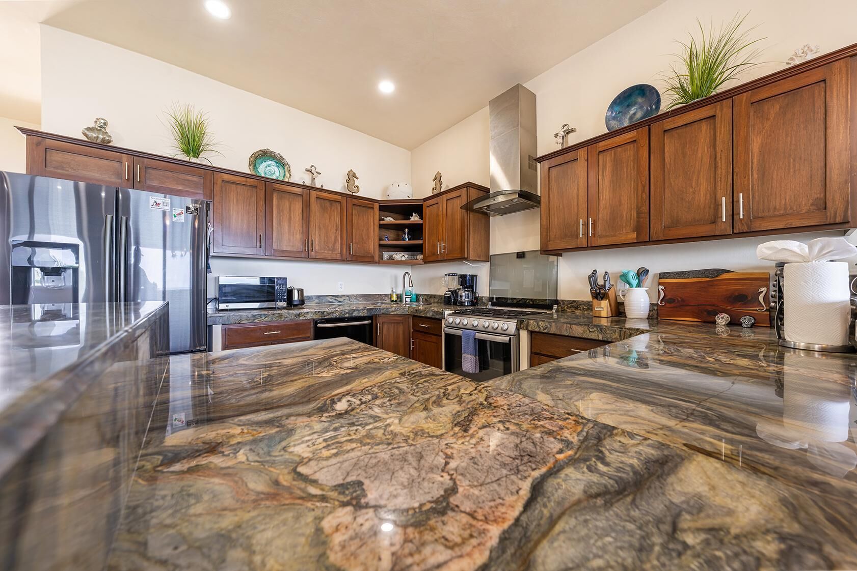 A modern kitchen with wooden cabinets, a granite countertop, stainless steel appliances, and decorative items.