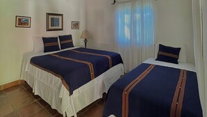 Una habitación con dos camas, ventilador de techo y ventana con cortinas.