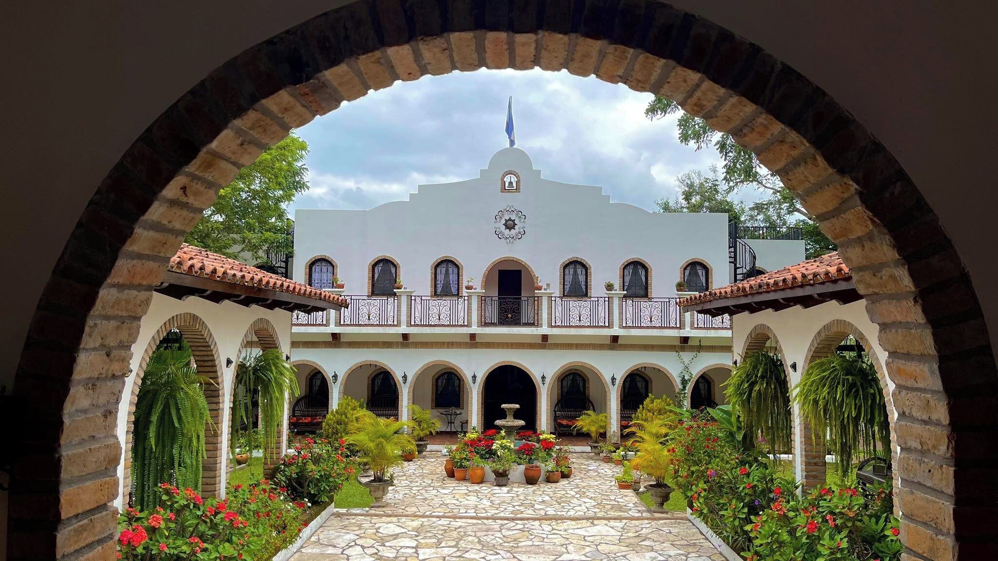 A courtyard with a white building, arched walkways, and potted plants.