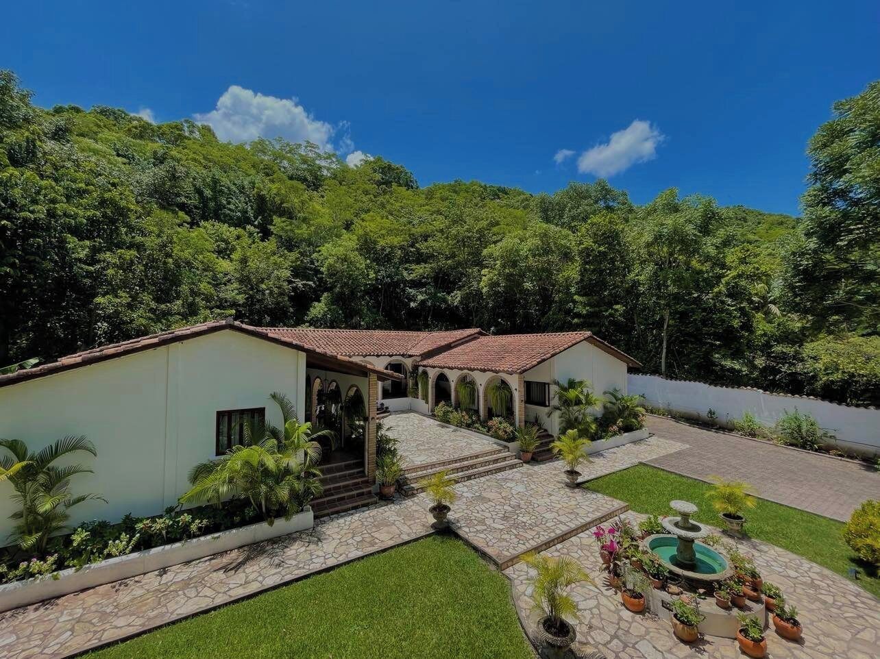 A two-story house with a tiled roof, a stone patio, and a small garden with a fountain.