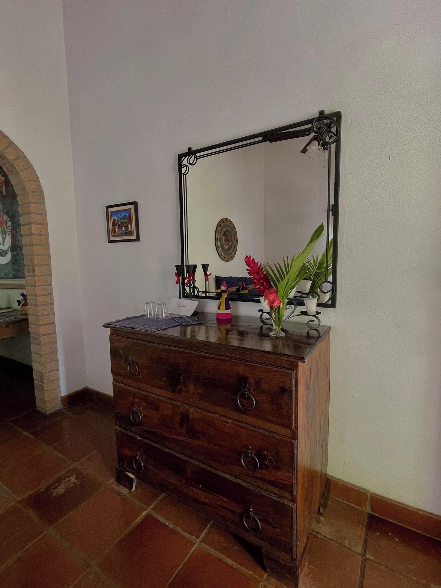 A wooden dresser with a mirror, a vase with flowers, and a small table with a picture frame and a candle.
