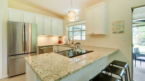 A kitchen with white cabinets, a stainless steel refrigerator, a granite countertop, a kettle, and a hanging light fixture. - 'Uncle Louie's' Gulf Coast Gem w/ Outdoor Oasis (Bradenton)