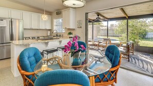 A modern kitchen with white cabinets, a stainless steel refrigerator, and a dining area with a glass table and blue chairs. - 'Uncle Louie's' Gulf Coast Gem w/ Outdoor Oasis (Bradenton)