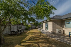 A backyard with a picnic table, a brick building, and a large air conditioning unit. - Rose's Beach Pad - Matarangi Holiday Home (Matarangi)