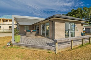 A modern house with a wooden deck, large sliding glass doors, and a covered patio area. - Rose's Beach Pad - Matarangi Holiday Home (Matarangi)