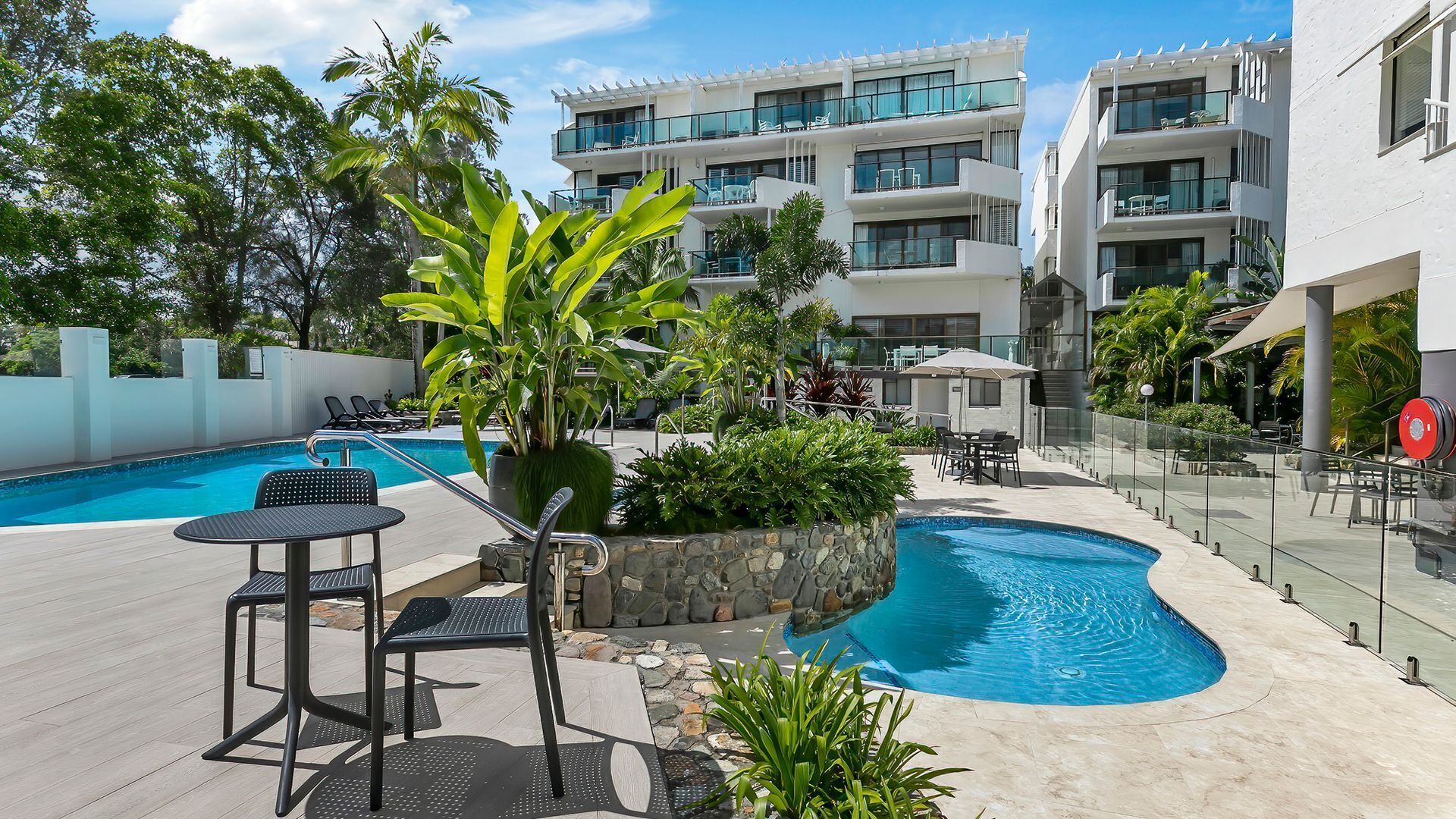 A swimming pool area with lounge chairs, a table, and a small garden.