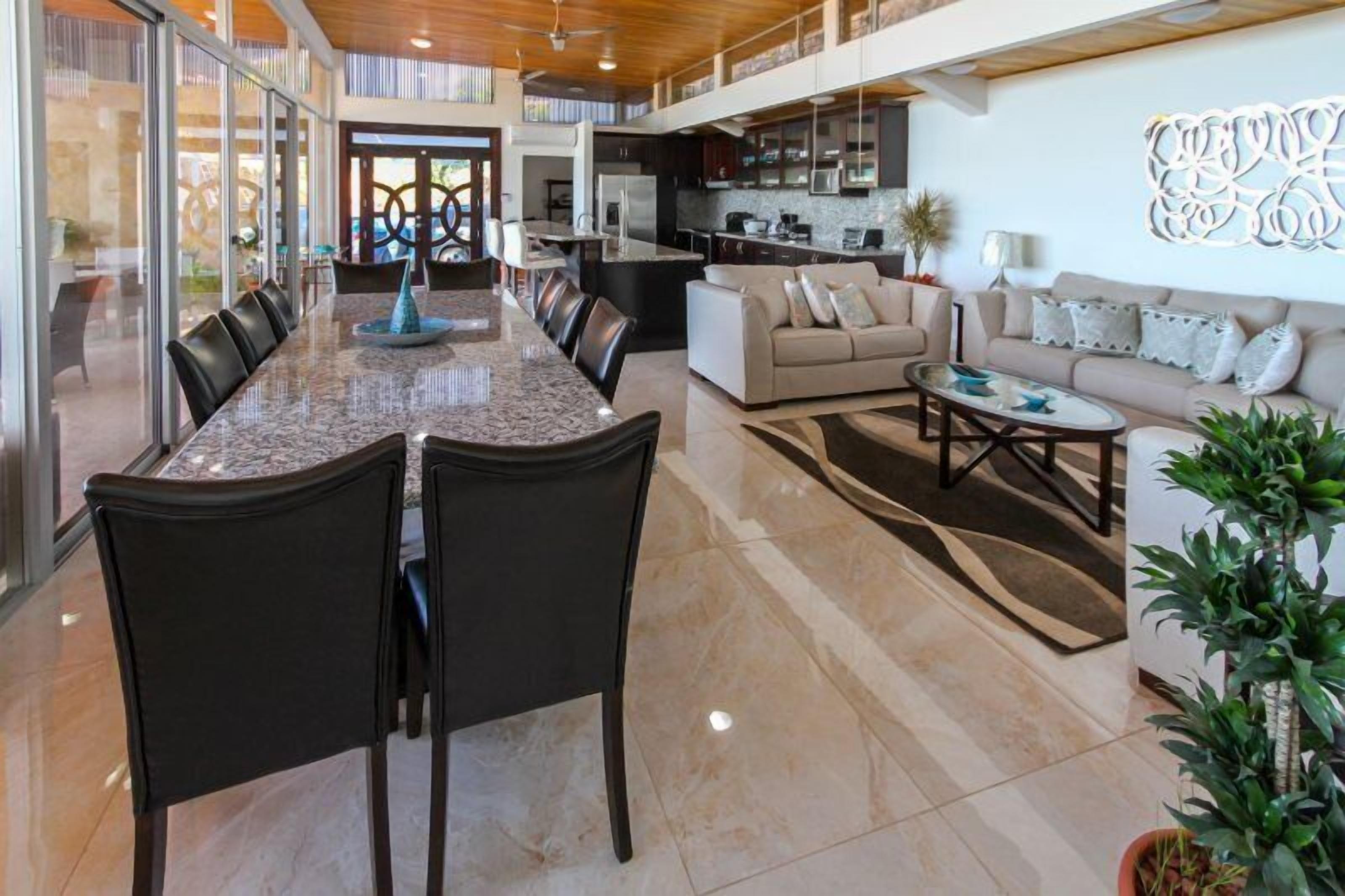 A spacious living area with a large dining table, comfortable seating, and a kitchen in the background.