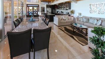 A spacious living area with a large dining table, comfortable seating, and a kitchen in the background.