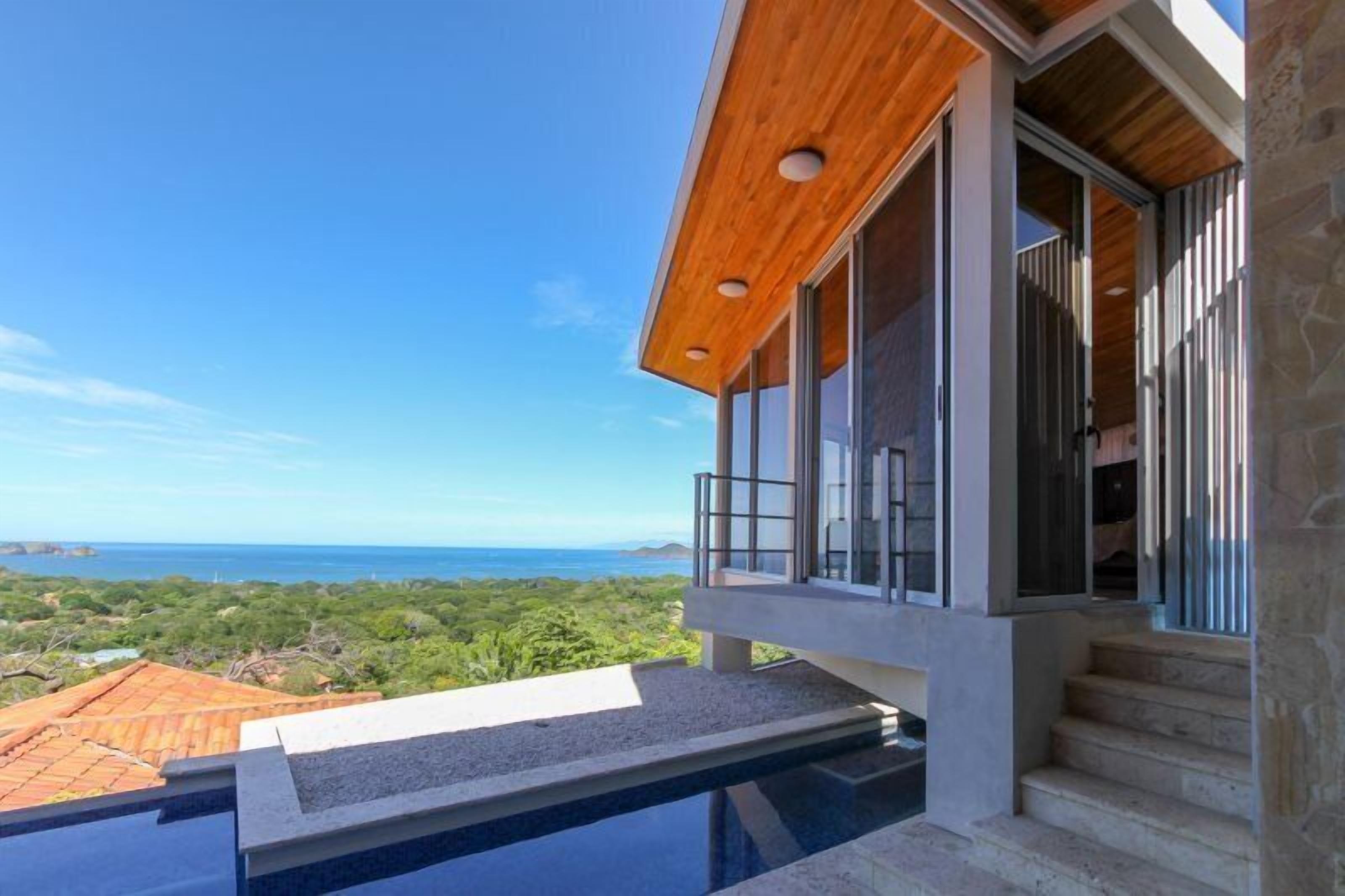 Une maison moderne avec une piscine, de grandes fenêtres et une vue sur l’océan.